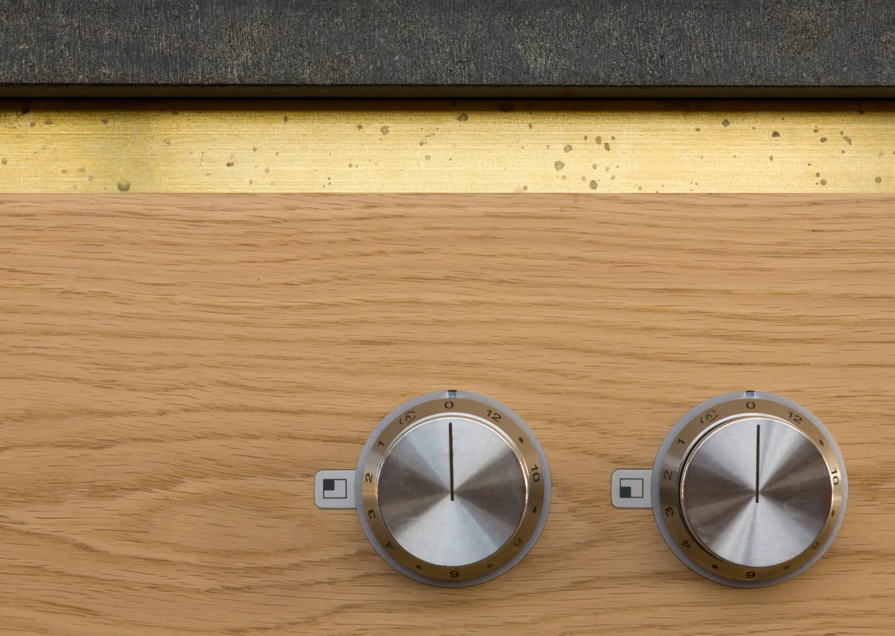 Detail of the kitchen island with integrated Gaggenau induction hob wrapped in Cathedral Oak Veneer, topped with a tooled edge brushed black granite countertop and brass handle strip. Refined kitchen simplicity.