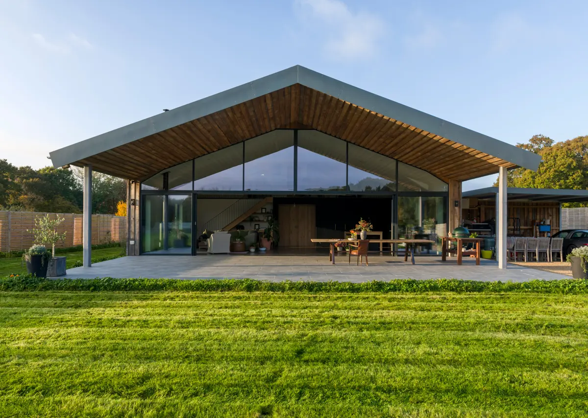 The rear of the contemporary Sussex barn showing its vaulted gleaming glass and steel structure and within the kitchen living space that opens out onto the large covered veranda.