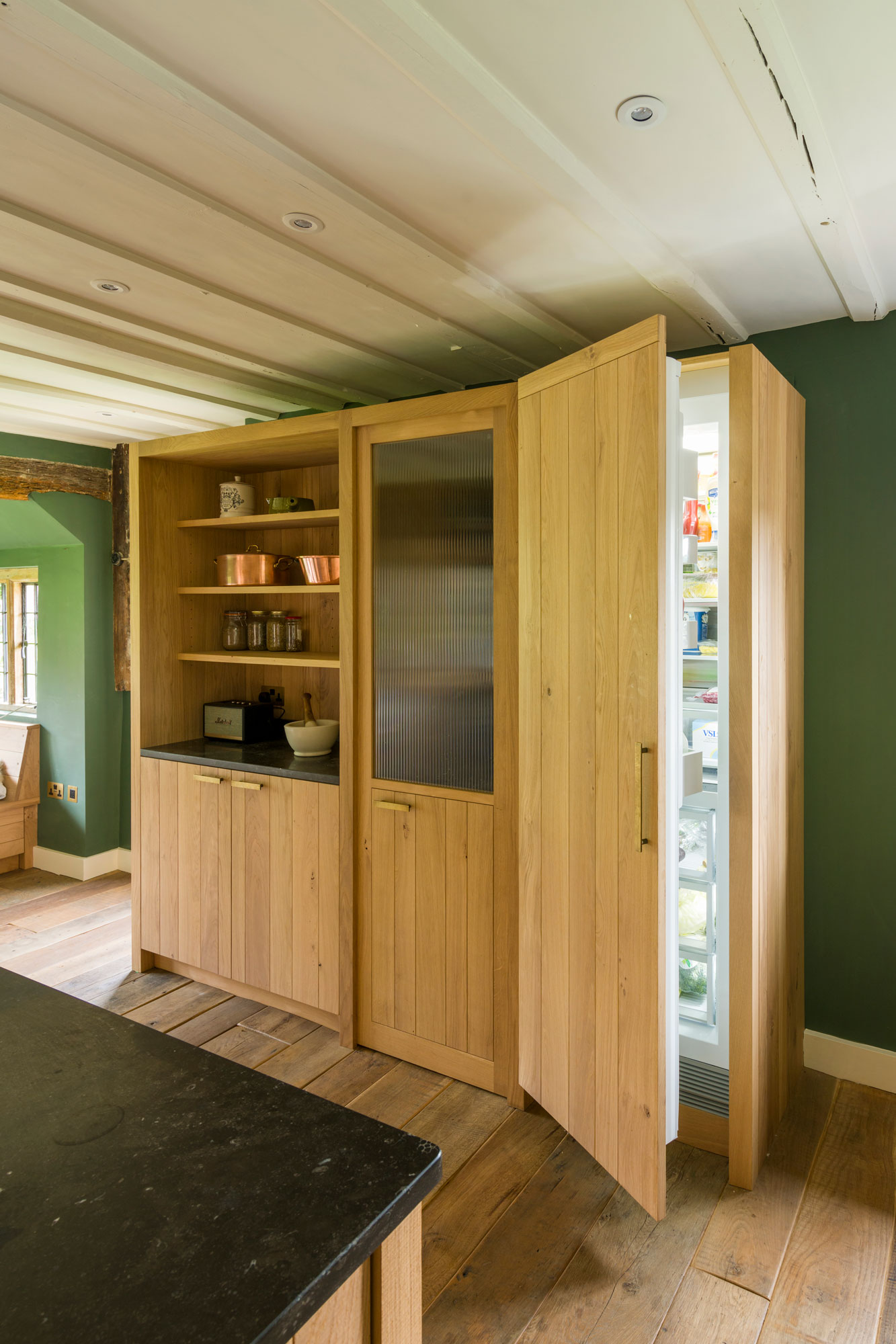 Band-sawn oak clad walls cleverly conceal a walk in pantry housed within an old inglenook and the family sized fridge-freezer.