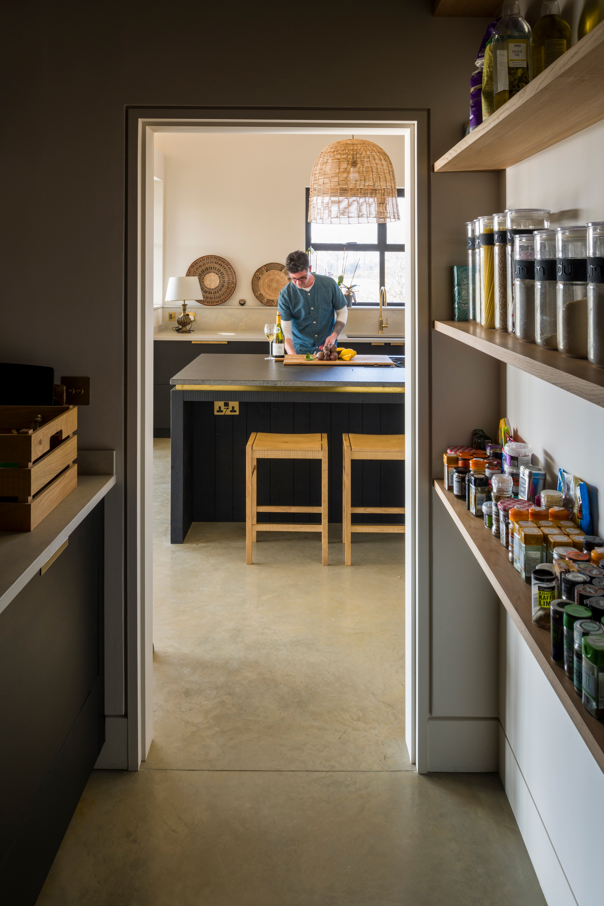 A walk in pantry with bespoke Richlite cabinetry and oak slatted pantry shelving on one side and oak shelving for storage jars on the other.