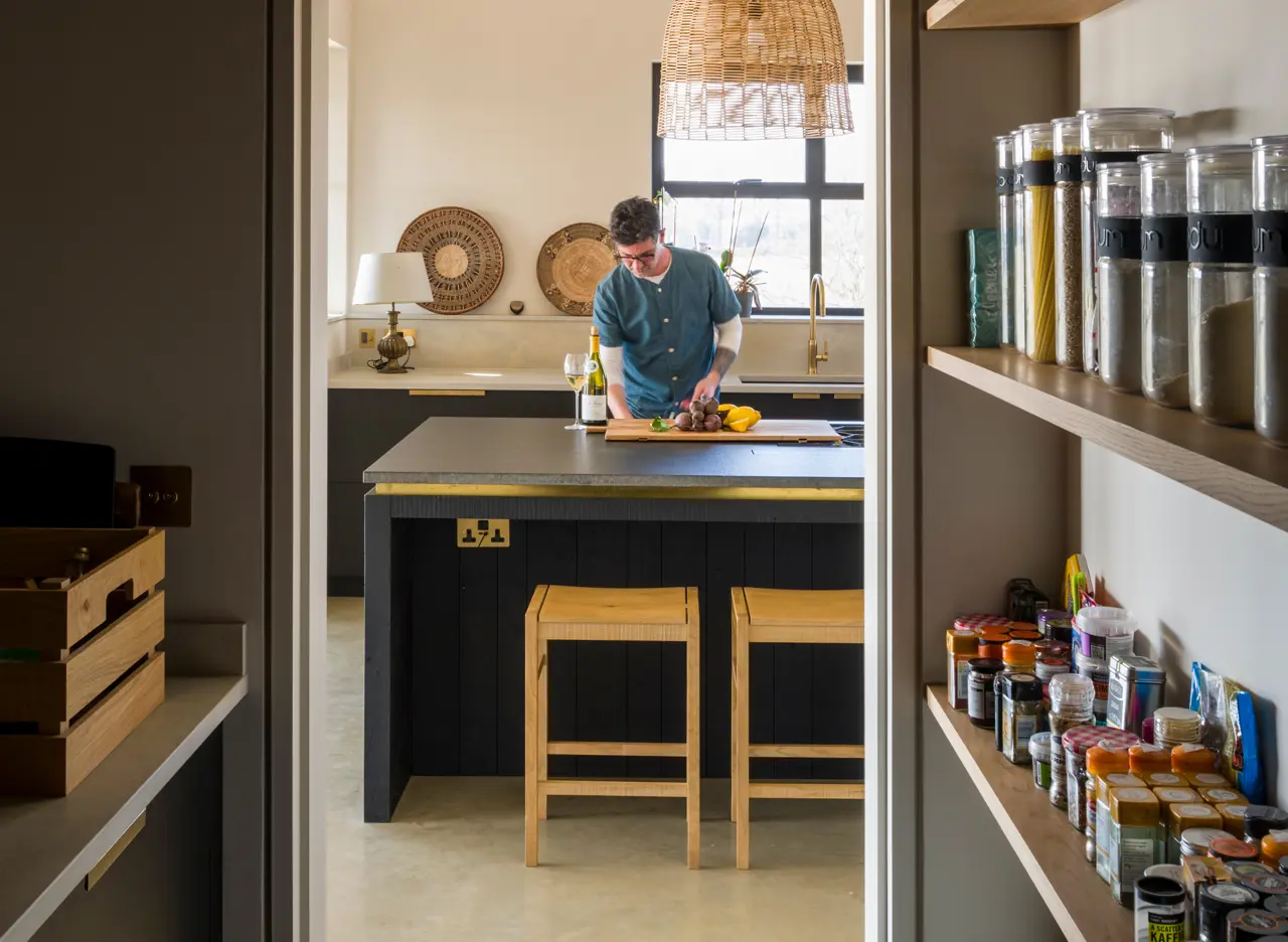 A walk in pantry with bespoke Richlite cabinetry and oak slatted pantry shelving on one side and oak shelving for storage jars on the other.