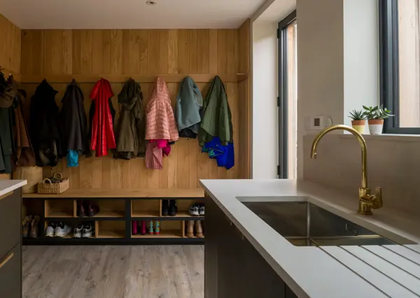 The utility room and boot room are hidden behind a pocket door clad in Blackened band-sawn oak and solid brass handle. Richlite and Topus concrete contrast with the raw oak panelling and traditional oak pegged coat rack.