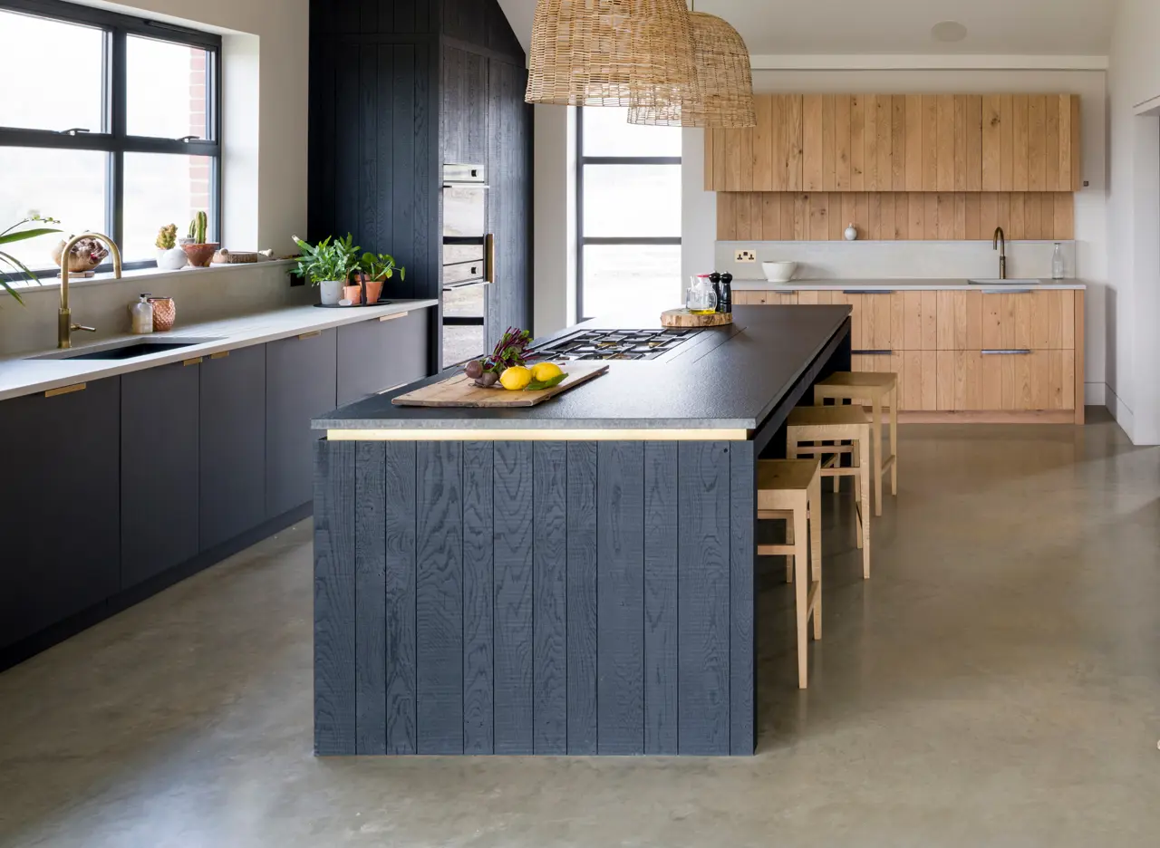 Bespoke contemporary kitchen featuring handcrafted blackened band-sawn oak and raw band-sawn oak set against a smooth Richlite sink cabinetry in front of a window with views over the Sussex Weald.