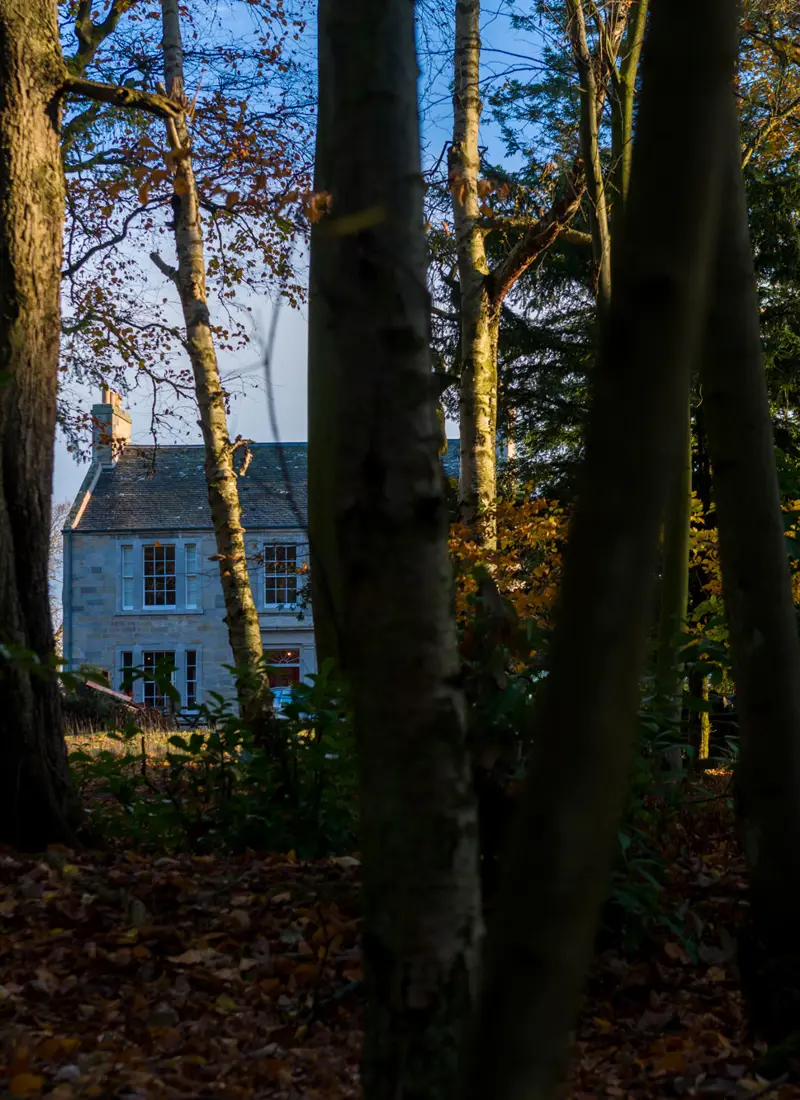 A serene Scottish country manor house, partially veiled by trees, exuding timeless charm and harmony with its surroundings.