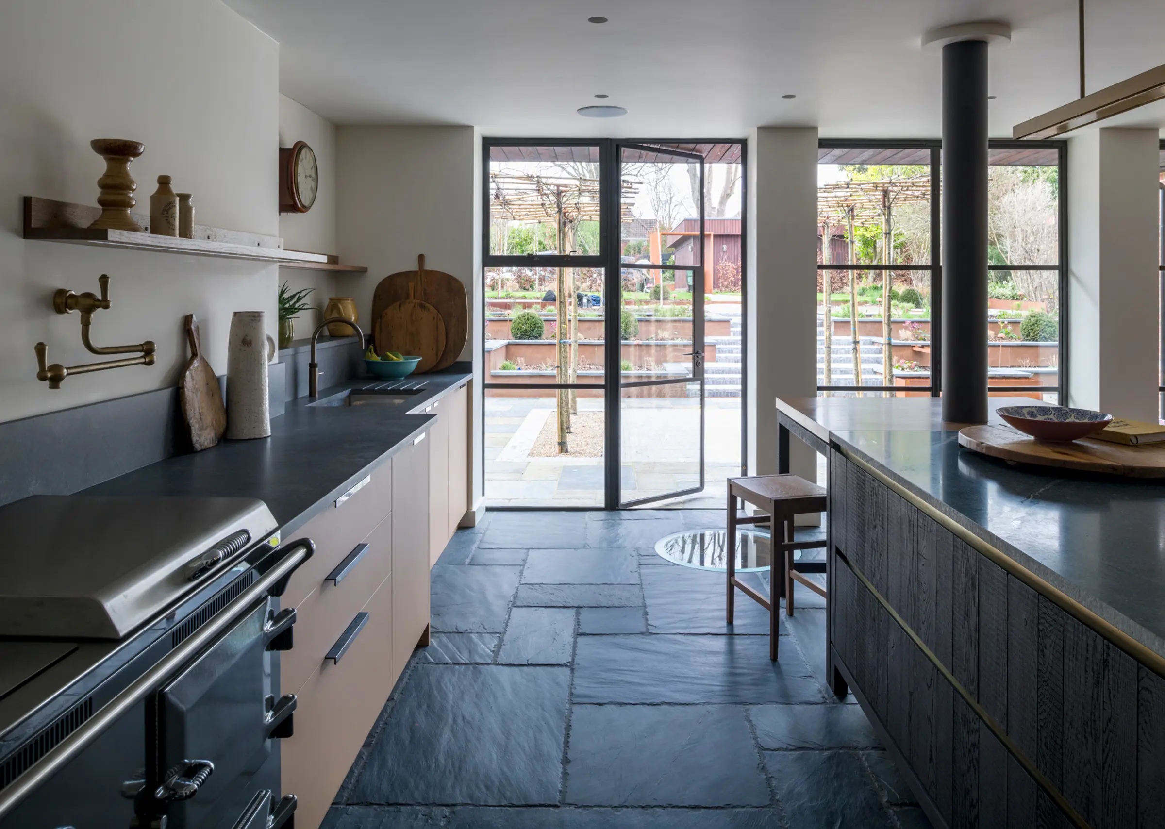 A close-up of bespoke kitchen cabinetry in Sandy Fenix next to a kitchen island in blackened band-sawn oak, paired with solid brass hardware for a touch of luxury kitchen feel.