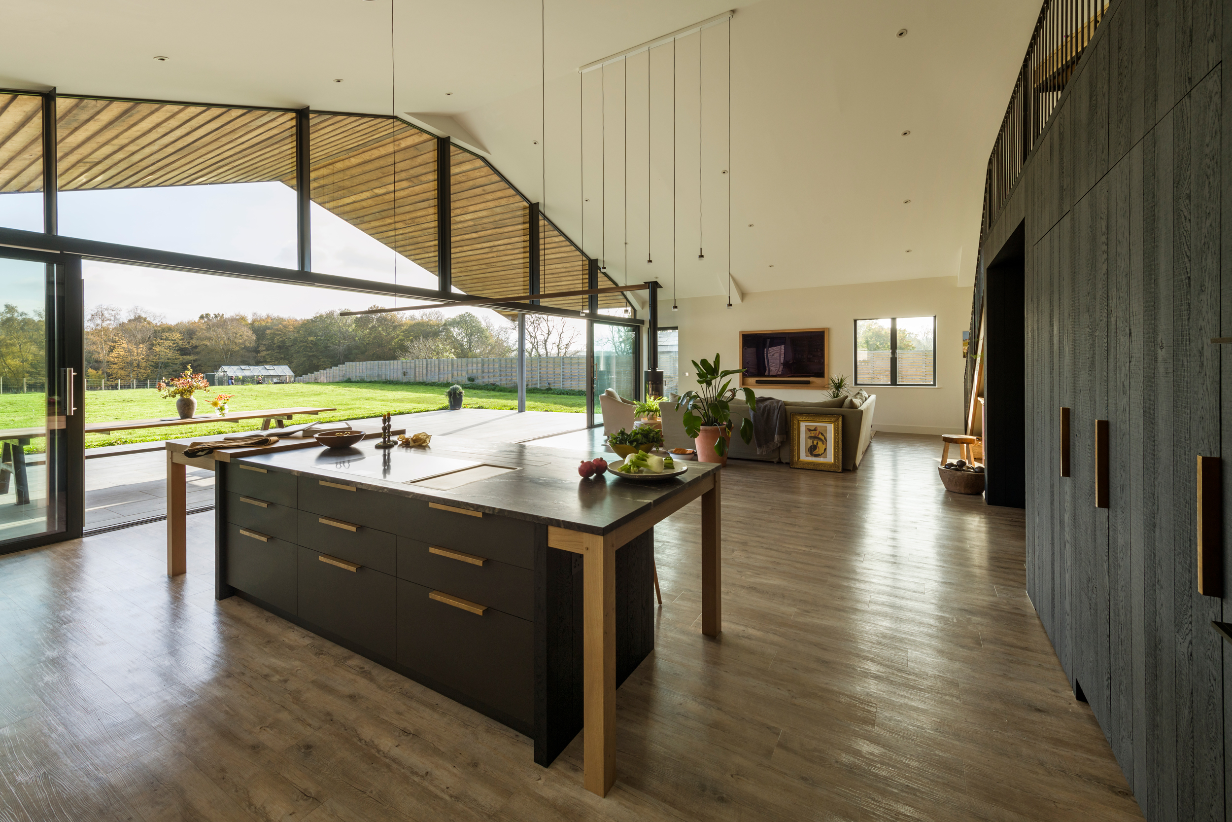 A large open plan kitchen and living space with a central bespoke kitchen island with integrated hob and stainless teppanyaki plate and seating areas for social kitchen gatherings.
