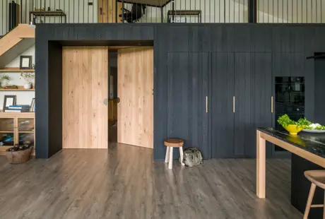 Bespoke double doors in solid oak open onto the open plan kitchen dining and living space. A wall of blackened band-sawn oak conceals bulky appliances in this bespoke contemporary kitchen.